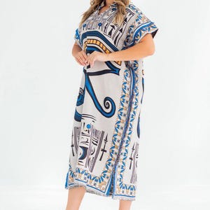 May include: A knee-length, short-sleeved dress with an Egyptian-inspired print in white, blue, black, and gold. The dress features a V-neck and a decorative border along the edges. The text "Every thread holds quality" is visible.