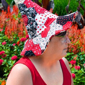 Pode incluir: Um chapéu acolchoado com uma copa alta e pontiaguda e uma aba larga e curva. O chapéu é feito de um mosaico de peças de tecido em vermelho, branco e preto, apresentando vários padrões, incluindo bolinhas, estampas florais e xadrez.