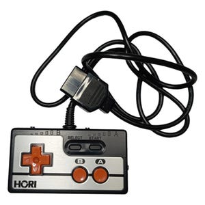 Könnte beinhalten: Ein schwarzer und silberner Videospiel-Controller mit orangefarbenen Knöpfen. Der Controller hat ein schwarzes Kabel mit einem Stecker am Ende. Auf dem Controller steht "HORI" gedruckt.