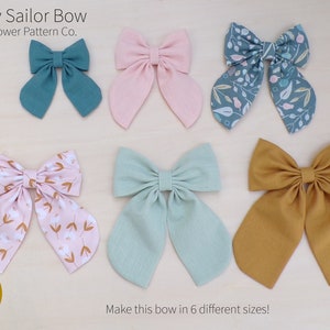 May include: Six different fabric bows in various colours and patterns, including teal, pink, green, and brown. The text "The Lily Sailor Bow by Wildflower Pattern Co." and "PDF Pattern" are visible at the top of the image. The text "Make this bow in 6 different sizes!" is visible at the bottom of the image.