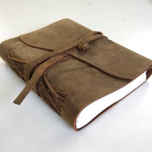 May include: A brown leather journal with a leather strap closure and a white paper insert. The journal has a rustic, vintage look.