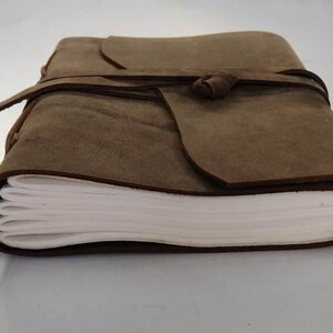May include: A brown leather-bound journal with a tied closure. The journal has blank pages and is closed.