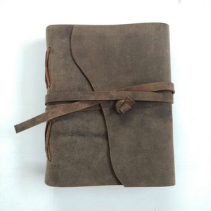 May include: A brown leather-bound journal with a rustic look. The journal is closed and tied with a brown leather strap.