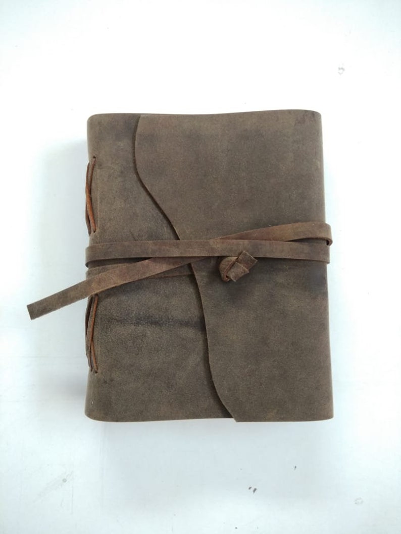 May include: A brown leather-bound journal with a rustic look. The journal is closed and tied with a brown leather strap.