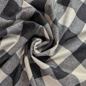 May include: Close-up of a fabric with a large black and white buffalo plaid pattern. The fabric is folded and draped, showing the texture and weave of the material. The pattern consists of large, evenly spaced squares.
