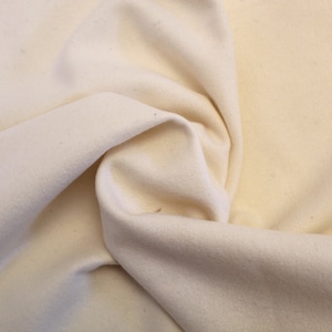May include: A close-up of a piece of off-white fabric, folded and textured, showing the soft, natural material.