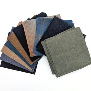 May include: A collection of square fabric swatches arranged in a fan shape. The pieces feature various textures and colors, including olive green, charcoal gray, navy blue, tan, brown, and black, with some showing subtle wood grain patterns.