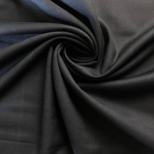 May include: Close-up of a dark navy blue fabric with a subtle grid pattern. The material is draped and swirled, creating soft folds and shadows. The texture appears smooth and possibly woven, suitable for apparel or home decor.