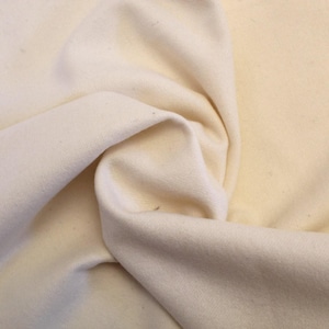 May include: A close-up of a piece of off-white fabric, folded and textured. The fabric is soft and smooth, with a subtle sheen.