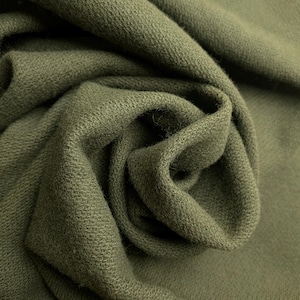 May include: A solid olive green fabric with a dense, textured weave. The material is draped in soft, organic folds, highlighting the consistent matte finish and the intricate, slightly raised pattern of the textile fibers across the surface.
