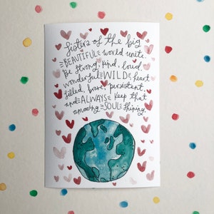 Könnte beinhalten: Aquarell-Grußkarte mit dem Text "Sisters of the big beautiful world unite". Die Karte zeigt eine Illustration eines blau-grünen Globus, umgeben von roten und rosa Herzen. Der Hintergrund hat bunte Tupfen.