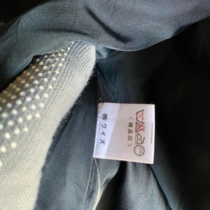 May include: Close-up of a garment's interior, showcasing a label with Japanese text and care symbols. The fabric appears to be a dark, possibly navy, color. The label is white with black text and symbols.