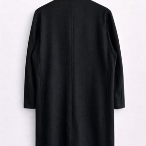 May include: A long, black coat hanging on a black hanger against a white background. The coat has a classic design with a notched collar and a single vent in the back. The coat's length extends to the mid-calf.
