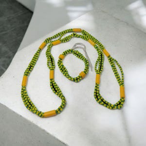 May include: A set of green and yellow beaded jewellery, including a necklace and a bracelet. The beads are arranged in a striped pattern.