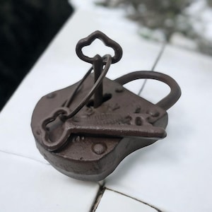 Peut inclure: Un cadenas en fonte de style vintage avec une clé attachée. Le cadenas est brun et a un trou de serrure en forme de cœur. La clé est également brune et a une tête en forme de nuage.