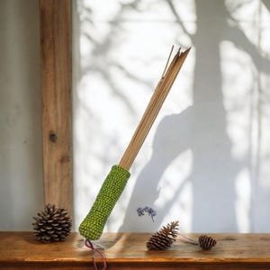 May include: A green and yellow beaded handle attached to a bundle of wooden sticks. The handle is decorated with a pattern of small green and yellow beads. The sticks are bundled together and extend out from the handle.