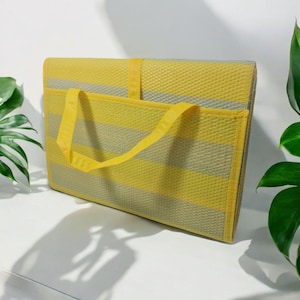 May include: A yellow and gray striped picnic mat with a yellow carrying handle. The mat is folded up and ready to be carried.