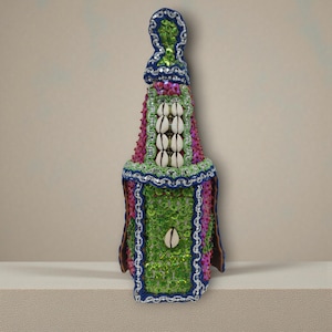 Può includere: Oggetto decorativo a forma di bottiglia con un design vibrante. Presenta una combinazione di colori verde, rosa e blu, adornato con paillettes e conchiglie. La parte superiore ha un cappuccio blu e il corpo è ornato da molteplici conchiglie.
