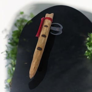 May include: A wooden flute with a red ribbon tied around it. The flute has four finger holes and a metal ring attached to the top.
