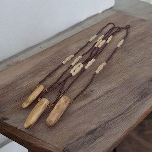 May include: A long necklace made of brown and white beads with three bone pendants hanging from it. The necklace is lying on a wooden surface.