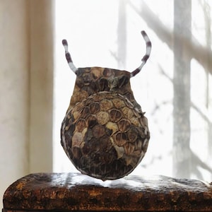 Può includere: Una borsa rotonda in pelle con un motivo marrone e bianco, con due lunghi cinturini sottili, bianchi e marroni, che si estendono dalla parte superiore.