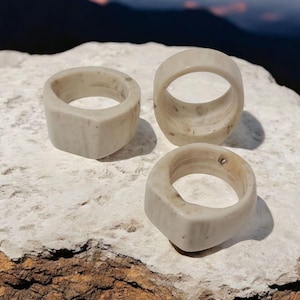 以下が含まれることがあります： 自然な木目模様の白い骨の指輪が3つ。指輪はすべてサイズと形が異なります。