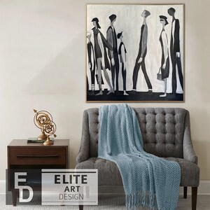May include: A black and white abstract painting of a group of people walking in a line. The painting is framed in a gold frame and is hanging on a white wall above a gray sofa with a blue throw blanket.