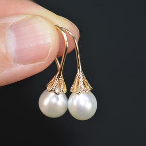 May include: A pair of gold dangle earrings with white pearl drops. The earrings feature a delicate, filigree design.