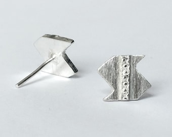May include: A pair of silver geometric stud earrings with a textured finish. The earrings are shaped like a chevron or arrowhead.