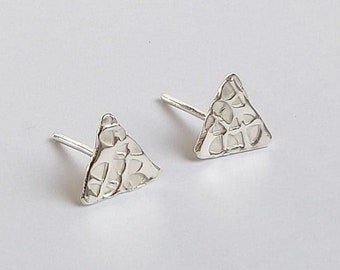 May include: A pair of small, silver-colored triangle stud earrings. The earrings have a textured surface and a post for insertion. The earrings are displayed on a white background.