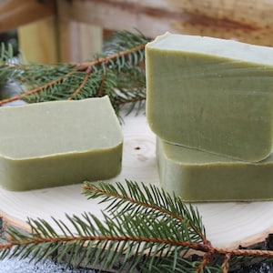 May include: Three bars of green soap on a wooden slice with a sprig of evergreen.