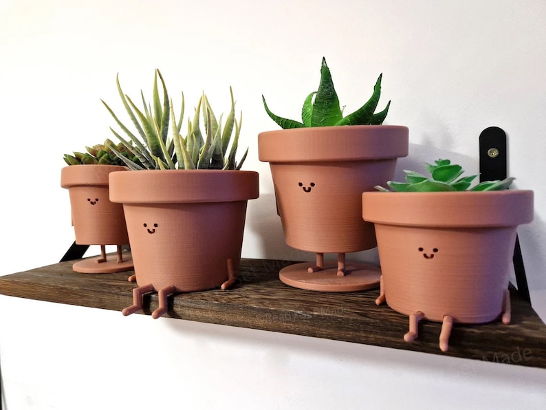 May include: Four terracotta pots with smiling faces and legs, holding various green plants. The pots are arranged on a wooden shelf.