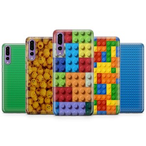 May include: Five different phone cases with various designs. One case is green with a textured pattern, another is yellow with a pattern of Lego heads, another is purple with a pattern of Lego bricks, another is yellow, orange, red, and blue with a pattern of Lego bricks, and the last case is blue with a textured pattern.