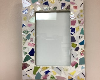 May include: A white picture frame with a mosaic design made of broken pieces of colorful ceramic tiles. The frame is rectangular and has a white background.