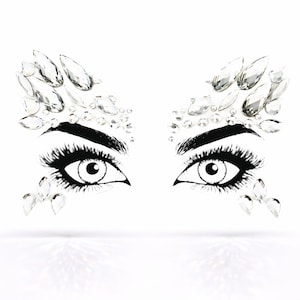 May include: A graphic illustration of two eyes with long eyelashes and thick, dark eyebrows. Clear, sparkling rhinestones are arranged around the eyes, creating a glamorous, decorative effect. The design is set against a clean white background.