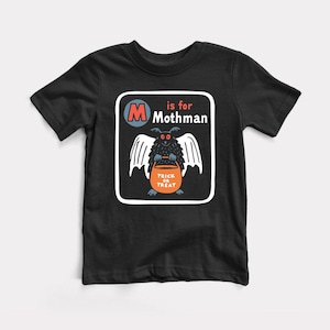 May include: A black short-sleeve t-shirt featuring a graphic print of a dark, winged creature with red eyes holding an orange pumpkin bucket. The text reads M is for Mothman and Trick or Treat, enclosed within a white rounded square border.