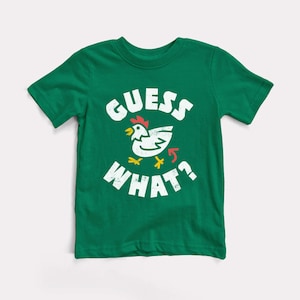 May include: Green short-sleeved t-shirt with a white graphic of a chicken and the text "GUESS WHAT?"
