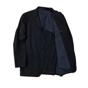 May include: A black blazer with a three-button closure and a notched lapel. The blazer's interior lining is a contrasting dark blue. The jacket is displayed open, revealing the inner construction and pockets. The garment is made of a smooth, solid fabric.