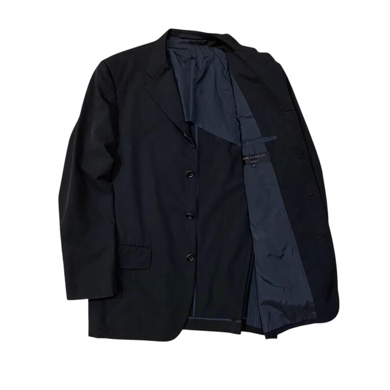May include: A black blazer with a three-button closure and a notched lapel. The blazer's interior lining is a contrasting dark blue. The jacket is displayed open, revealing the inner construction and pockets. The garment is made of a smooth, solid fabric.