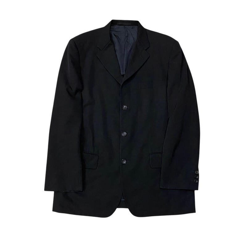 May include: A black blazer with a three-button closure and two front pockets. The blazer has a notched lapel and long sleeves. The interior lining is a dark blue color. The blazer is a classic style.