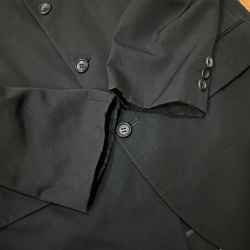 May include: Black blazer with three buttons on the sleeve and several buttons on the front. The blazer is made of a smooth fabric and has a tailored fit. The buttons are a dark color and match the blazer.