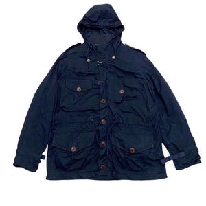 May include: A navy blue hooded jacket with multiple front pockets and wooden toggle closures. The jacket features a drawstring waist and adjustable cuffs. The garment has a classic military-inspired design.