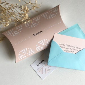 Puede incluir: Una caja de regalo rosa claro y una tarjeta de visita a juego con dise&ntilde;os geom&eacute;tricos blancos y el texto "terram CREAZIONI DI SARDEGNA". Un sobre azul claro contiene una tarjeta con texto en italiano.