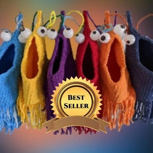 May include: Six colorful crocheted bird nests with googly eyes and fringe. The nests are hanging from a string and are arranged in a rainbow pattern. The text "BEST SELLER" is displayed on a gold star.