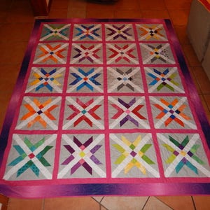 May include: A colorful quilt with a geometric pattern of stars and squares. The quilt is made of various fabrics in shades of pink, purple, blue, green, yellow, orange, and white. The quilt is laid out on a tiled floor.