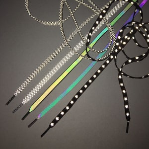 Puede incluir: Surtido de cordones reflectantes en varios colores y patrones, incluyendo negro con estrellas blancas, iridiscente y a cuadros.