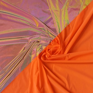 Peut inclure: Deux morceaux de tissu, l'un iridescent et l'autre orange vif, sont drapés l'un sur l'autre. Le tissu iridescent a un reflet rose, violet et vert.