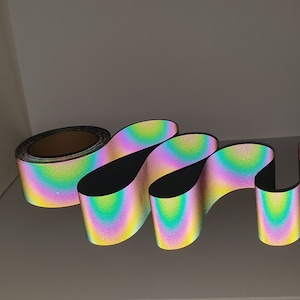 May include: A roll of iridescent rainbow reflective tape. The tape is folded into a series of loops, showing the rainbow effect.