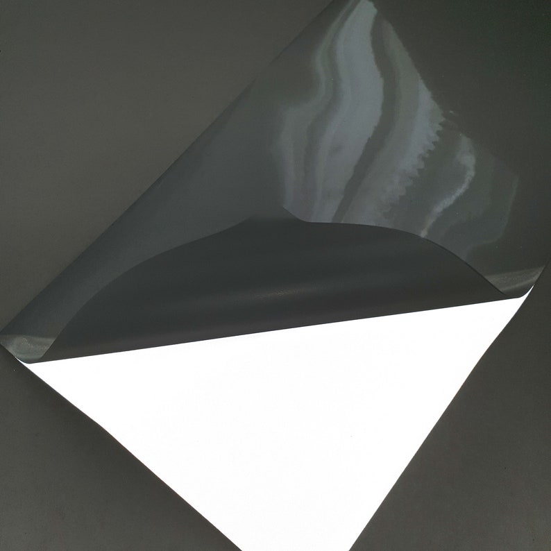 May include: A sheet of white adhesive vinyl with a black backing. The backing is peeled back to reveal the adhesive side of the vinyl.