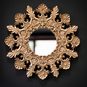 May include: An ornate gold-toned mirror with a round reflective surface. The mirror is surrounded by a decorative frame with intricate details.